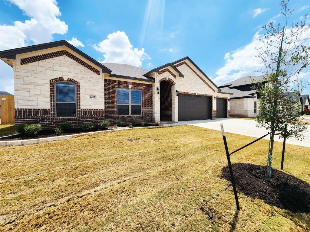 Carothers Executive Homes Aria plan brick exterior with 3-car garage at 607 Golden Eagle in Salado, Texas